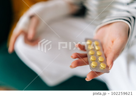 Close-up cropped shot of unrecognizable suffering from pain young woman with broken right hand wrapped in gypsum bandage holding blister packs of pills. Concept of insurance and healthcare. Close-up cropped shot of unrecognizable suffering from pain young woman with broken right hand wrapped in gypsum bandage holding blister packs of pills. Concept of insurance and healthcare. 102259621