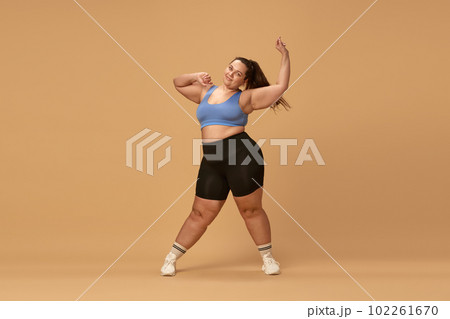 Young overweight woman training in sportswear against brown studio background. Losing weight with fitness and diet Young overweight woman training in sportswear against brown studio background. Losing weight with fitness and diet 102261670