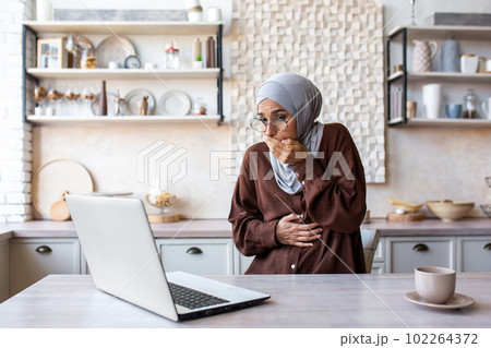 Arab young woman in hijab is pregnant and working on a laptop. She feels bad, feels strong nausea, urges to vomit, covers her mouth with her hand, symptoms of pregnancy. Arab young woman in hijab is pregnant and working on a laptop. She feels bad, feels strong nausea, urges to vomit, covers her mouth with her hand, symptoms of pregnancy. 102264372