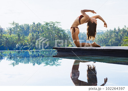 Active woman in bikini stretching at poolside to keep fit 102264397