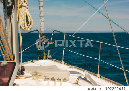 A sea voyage on a sunny, warm day. The bow of a yacht ship, ship's ropes. Yachting, nautical tourism. Marine landscape. The hills against blue sky and blue sea ocean water. Summer holidays trip. A sea voyage on a sunny, warm day. The bow of a yacht ship, ship's ropes. Yachting, nautical tourism. Marine landscape. The hills against blue sky and blue sea ocean water. Summer holidays trip. 102265051
