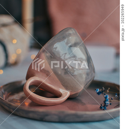 Cozy still life composition featuring a ceramic tree glowing with warm light and a soft pink and gray mug and saucer Cozy still life composition featuring a ceramic tree glowing with warm light and a soft pink and gray mug and saucer 102265949