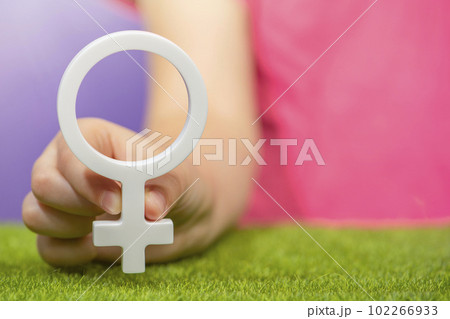 The concept of gender. Female gender symbol in hand on purple background in pink t-shirt with copy space 102266933