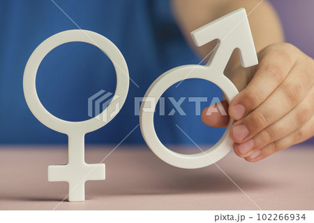 The concept of gender equality. Symbol of female and male gender in hand as a symbol of equality of rights. On a purple background in a blue t-shirt with copy space 102266934