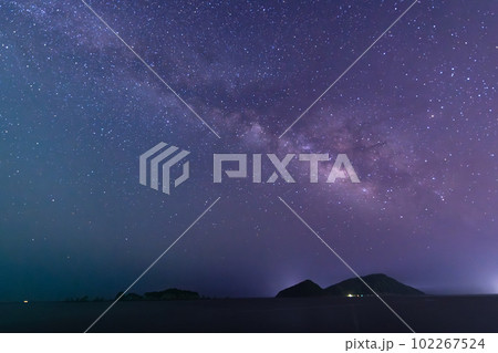 宮崎県日南市猪崎鼻から七つ岩と並ぶ大島の上に広がる星空に横に流れる天の川と灯台と共に海を照らす金星 102267524