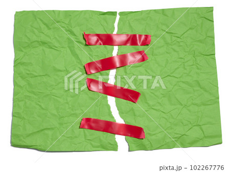 A torn green sheet of paper is fastened with red sticky tape on a white background 102267776