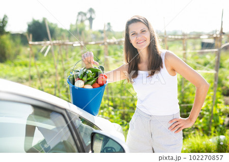 Happy woman puts basket with ripe vegetables in car 102270857