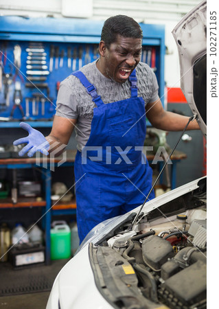 Displeased auto mechanic stands next to a car in car service Displeased auto mechanic stands next to a car in car service 102271185