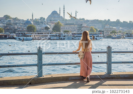 Young woman traveler in pinc dress enjoying great view of the Bosphorus and lots of seagulls in Istanbul 102273143