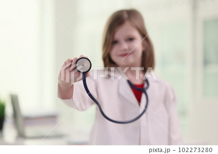 Adorable girl in white lab coat holds stethoscope in hand 102273280