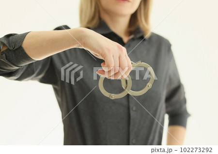 Woman in grey shirt holds iron handcuffs on beige background 102273292
