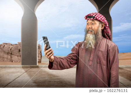 Muslim man with a beard wearing keffiyeh with agal using mobile phone 102276131