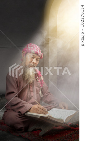 Muslim man with a beard wearing keffiyeh with agal sitting and reading the Quran Muslim man with a beard wearing keffiyeh with agal sitting and reading the Quran 102276134