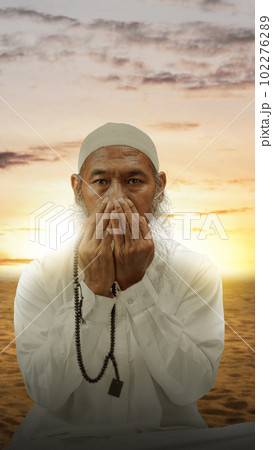 Muslim man with a beard wearing a white cap praying with prayer beads on his hands Muslim man with a beard wearing a white cap praying with prayer beads on his hands 102276289