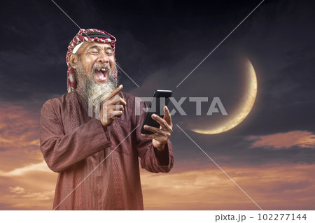 Muslim man with a beard wearing keffiyeh with agal using a mobile phone 102277144