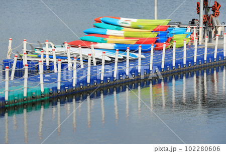Multicolored canoes on the dock at the lake with reflections on the water Multicolored canoes on the dock at the lake with reflections on the water 102280606