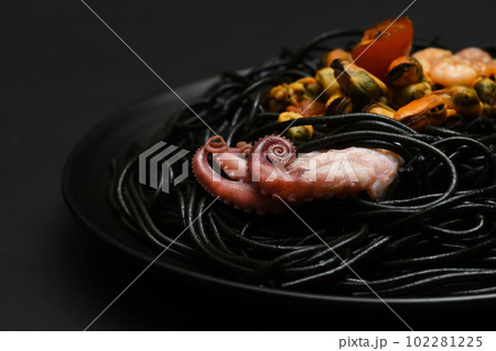 Black seafood pasta close up. Black squid inked spaghetti in black bowl on a dark background with shrimps, tomato, muscle and squid. 102281225