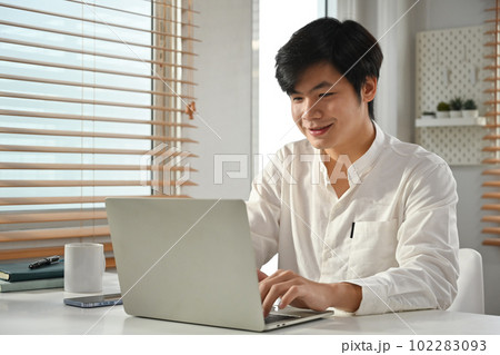 Portrait of smiling asian male entrepreneur sitting in modern office and using laptop. Business technologies concept Portrait of smiling asian male entrepreneur sitting in modern office and using laptop. Business technologies concept 102283093
