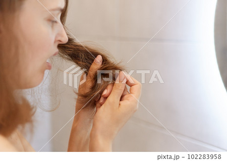 Closeup profile portrait of upset astonished woman looking at her dry hair, having problems, needs to change shampoo or special treatment at trichological clinic. 102283958