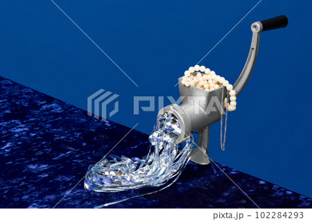 Portrait with meat grinder for cooking food full of pearl, jewelry over dark blue studio background. Rich people menu Portrait with meat grinder for cooking food full of pearl, jewelry over dark blue studio background. Rich people menu 102284293