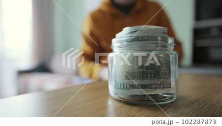Man putting a roll of money in a glass jar. Family saving money. Money box. 102287873