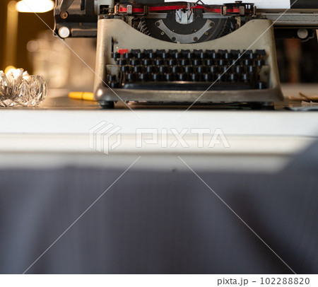 Old-fashioned typewriter on desk with ashtray and blurry jacket Old-fashioned typewriter on desk with ashtray and blurry jacket 102288820