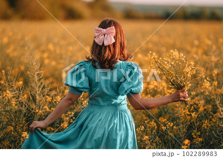 Unrecognizable woman in yellow canola flowers field.Lady in retro dress. Harvest 102289983