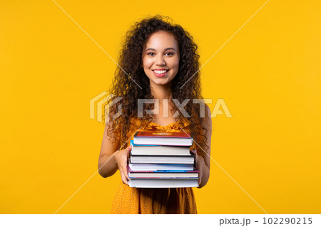 Happy student woman with stack of books from library on yellow background 102290215
