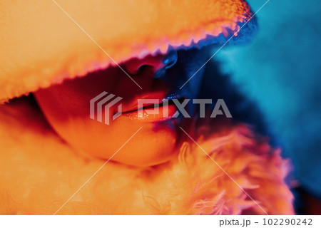 Shiny gloss on plump lips. Neon light. Woman in winter outfit, bucket hat 102290242