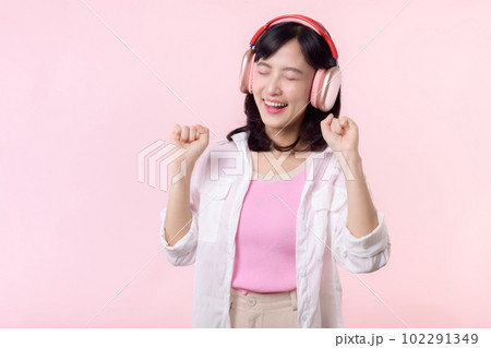 Smile pretty asian model person listen music song and enjoy dance with wireless headphone online audio radio sound. Positive fun exited joyful youth female woman on pink isolated background studio 102291349