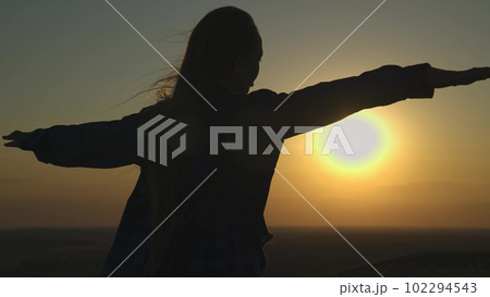 young girl looks at sunset and prays, religious person, her hair is flying in wind in glare of the sun, to believe in goodness, a woman's dream of love, to think and ask for forgiveness from heaven 102294543