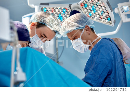Group of surgeons doing surgery in hospital operating theater, international medical team doing critical operation 102294752
