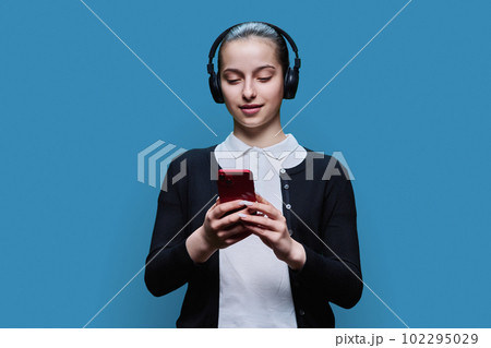 Young female in headphones listening audio, with smartphone on blue background Young female in headphones listening audio, with smartphone on blue background 102295029