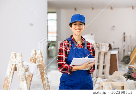 Woman in blue overalls checking completed construction work on drawing 102299513