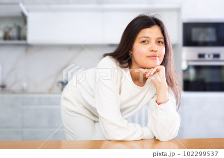Relaxed young brunette leaning on table in home kitchen Relaxed young brunette leaning on table in home kitchen 102299537