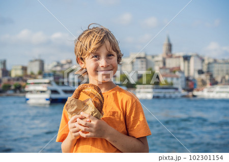 Boy in Istanbul having breakfast with Simit and a glass of Turkish tea. Glass of Turkish tea and bagel Simit against golden horn bay and the Galata Tower in Istanbul, Turkey. Turkiye. Traveling with 102301154
