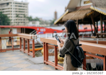 Young Asian woman backpack traveler using mobile phone in express boat pier on Chao Phraya River in Bangkok. 102305307