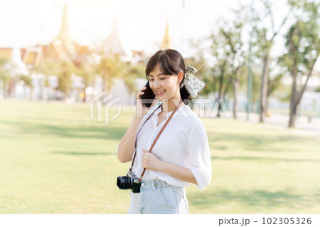 Portrait beautiful young asian woman with smartphone on summer holiday vacation trip with the grand palace in a background at Bangkok, Thailand Portrait beautiful young asian woman with smartphone on summer holiday vacation trip with the grand palace in a background at Bangkok, Thailand 102305326