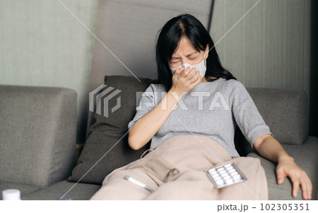 Sick asian woman with face mask having cough on sofa bed at home. Sick asian woman with face mask having cough on sofa bed at home. 102305351