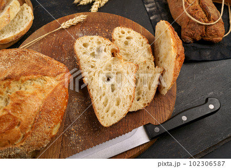 Fresh bread slice and cutting knife on rustic table Concept of homemade bread, natural farm products, domestic production. Healthy and tasty organic food. Round loaf of freshly baked sourdough bread Fresh bread slice and cutting knife on rustic table Concept of homemade bread, natural farm products, domestic production. Healthy and tasty organic food. Round loaf of freshly baked sourdough bread 102306587