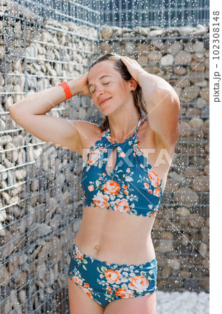 Beautiful woman, wearing swimsuit, taking shower in outdoor in her summer holidays 102308148
