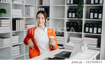 Confident business expert attractive smiling young woman typing laptop ang holding digital tablet on desk in office.. Confident business expert attractive smiling young woman typing laptop ang holding digital tablet on desk in office.. 102309615