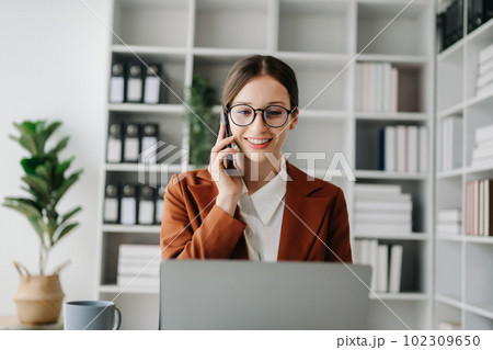 Business Caucasian woman Talking on the phone and using a laptop with a smile while sitting at modern office 102309650