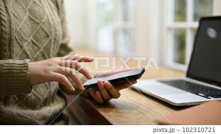 A woman in cozy sweater using her smartphone at her workspace. 102310721