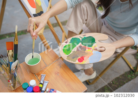 Creative art concept, Female artist is washing paintbrush while painting art on canvas in garden Creative art concept, Female artist is washing paintbrush while painting art on canvas in garden 102312030