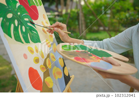 Outdoor activity concept, Female artist holds color palette and brush to painting picture on canvas Outdoor activity concept, Female artist holds color palette and brush to painting picture on canvas 102312041