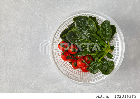 Washed green leaves of spinach and cherry tomatoes on a branch in a plastic white colander on a light stone table Washed green leaves of spinach and cherry tomatoes on a branch in a plastic white colander on a light stone table 102316385
