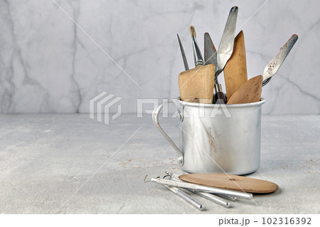 Variety of tools for sculpting and modeling in an aluminum cup and on a light stone background Variety of tools for sculpting and modeling in an aluminum cup and on a light stone background 102316392
