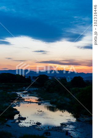 住宅街と山並みと川面をオレンジに染める春の夕焼 102316446