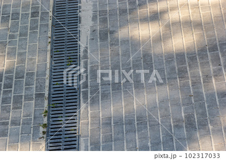 A lattice of a drainage paving system on a footpath made of square stone tiles, close up of a rainwater drainage system A lattice of a drainage paving system on a footpath made of square stone tiles, close up of a rainwater drainage system 102317033